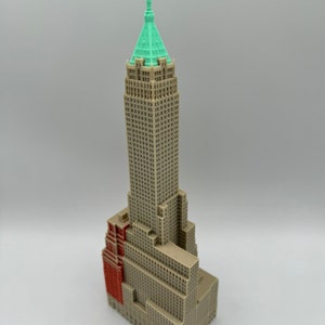 May include: A detailed model of a tall, beige skyscraper with a green roof. The building has a red brick section on the side.