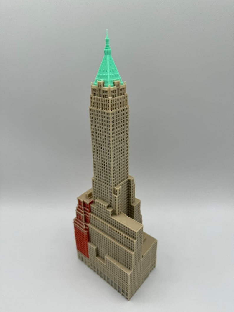 May include: A detailed model of a tall, beige skyscraper with a green roof. The building has a red brick section on the side.