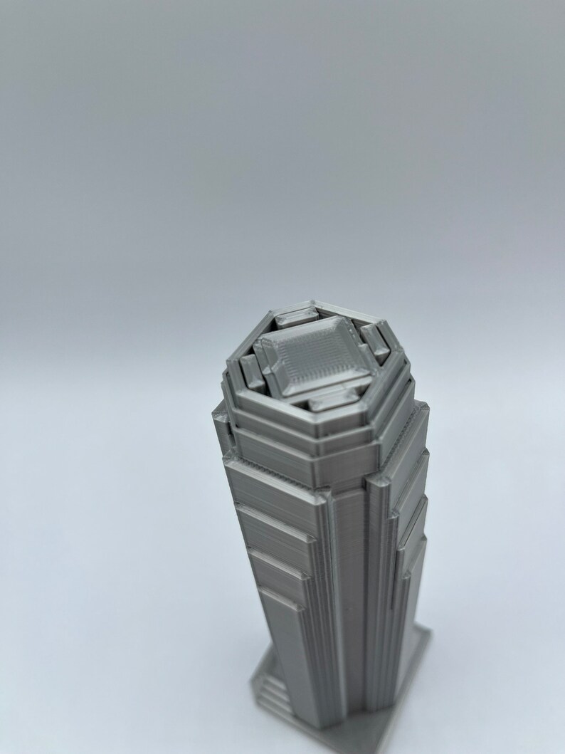 May include: A 3D printed model of a skyscraper with a hexagonal base and a layered design. The model is made of a silver-colored material.