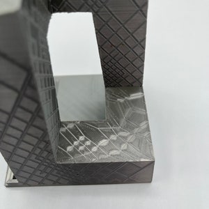 Peut inclure: Un objet gris imprim&eacute; en 3D avec un motif g&eacute;om&eacute;trique. L'objet a une forme rectangulaire avec une ouverture carr&eacute;e sur un c&ocirc;t&eacute;.