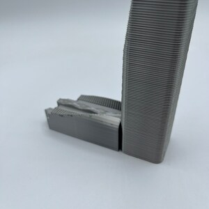 May include: A 3D printed model of a tall building with a textured surface. The model is made of gray plastic and has a rectangular base.
