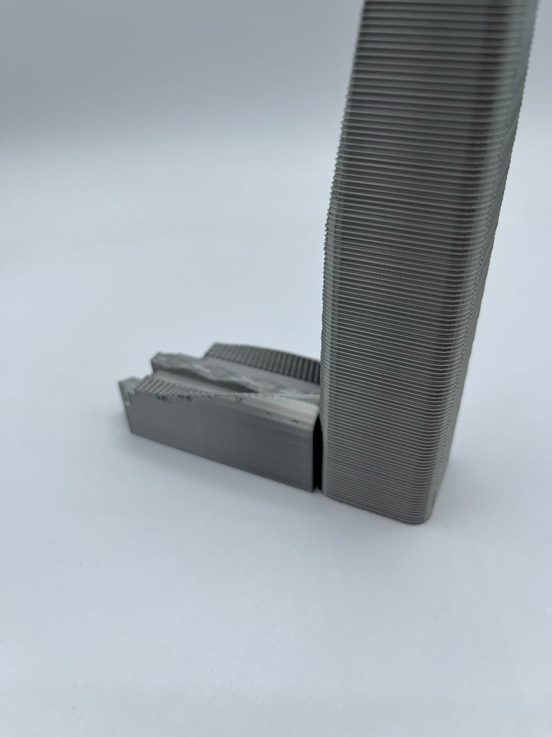 May include: A 3D printed model of a tall building with a textured surface. The model is made of gray plastic and has a rectangular base.