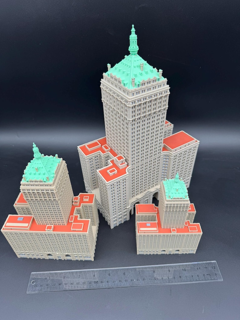 May include: A collection of miniature building models. The buildings are light gray with red rooftops and green accents. A ruler is placed in front of the models for scale.