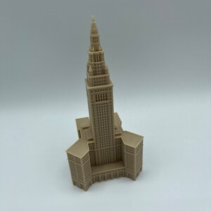May include: A beige 3D printed model of a tall building with a pointed roof. The building has many windows and a detailed facade.