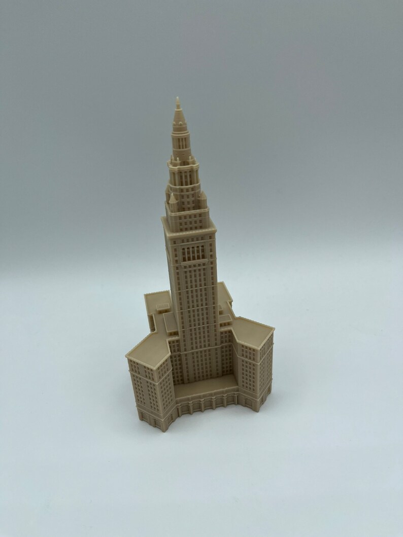 May include: A beige 3D printed model of a tall building with a pointed roof. The building has many windows and a detailed facade.