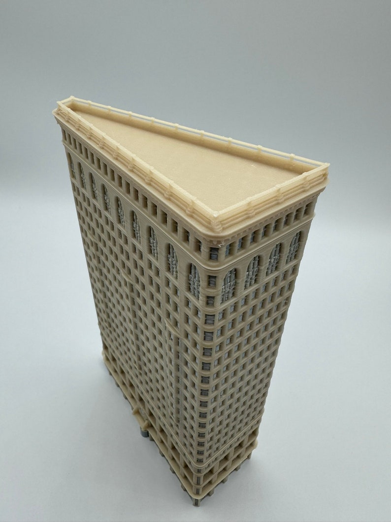 May include: A beige model of the Flatiron Building in New York City. The model is made of plastic and has a detailed facade with windows and decorative elements.