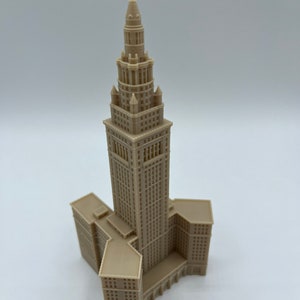 May include: A beige 3D printed model of a tall building with a pointed roof and a Y-shaped base.