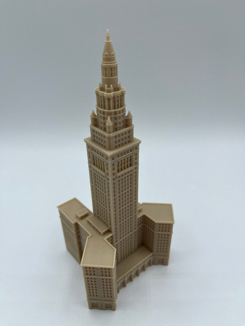 May include: A beige 3D printed model of a tall building with a pointed roof and a Y-shaped base.