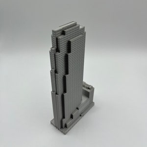 May include: A gray 3D printed model of a skyscraper with a rectangular base and a tall, narrow tower. The tower has a series of setbacks and a flat roof.