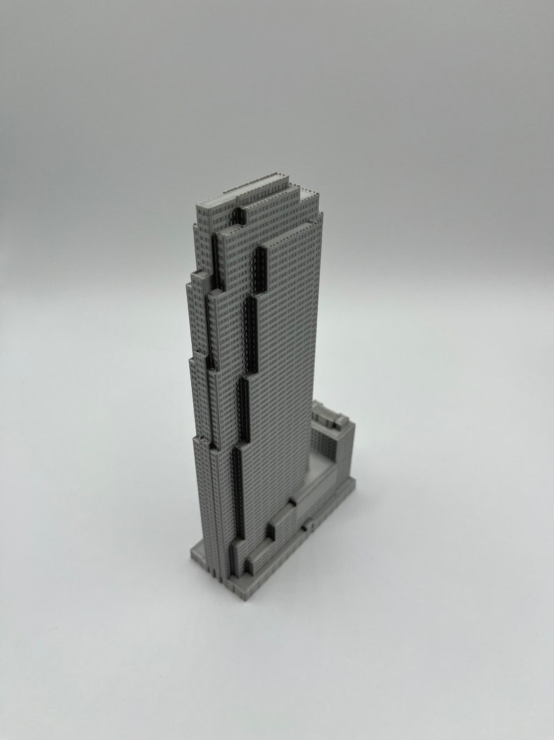May include: A gray 3D printed model of a skyscraper with a rectangular base and a tall, narrow tower. The tower has a series of setbacks and a flat roof.