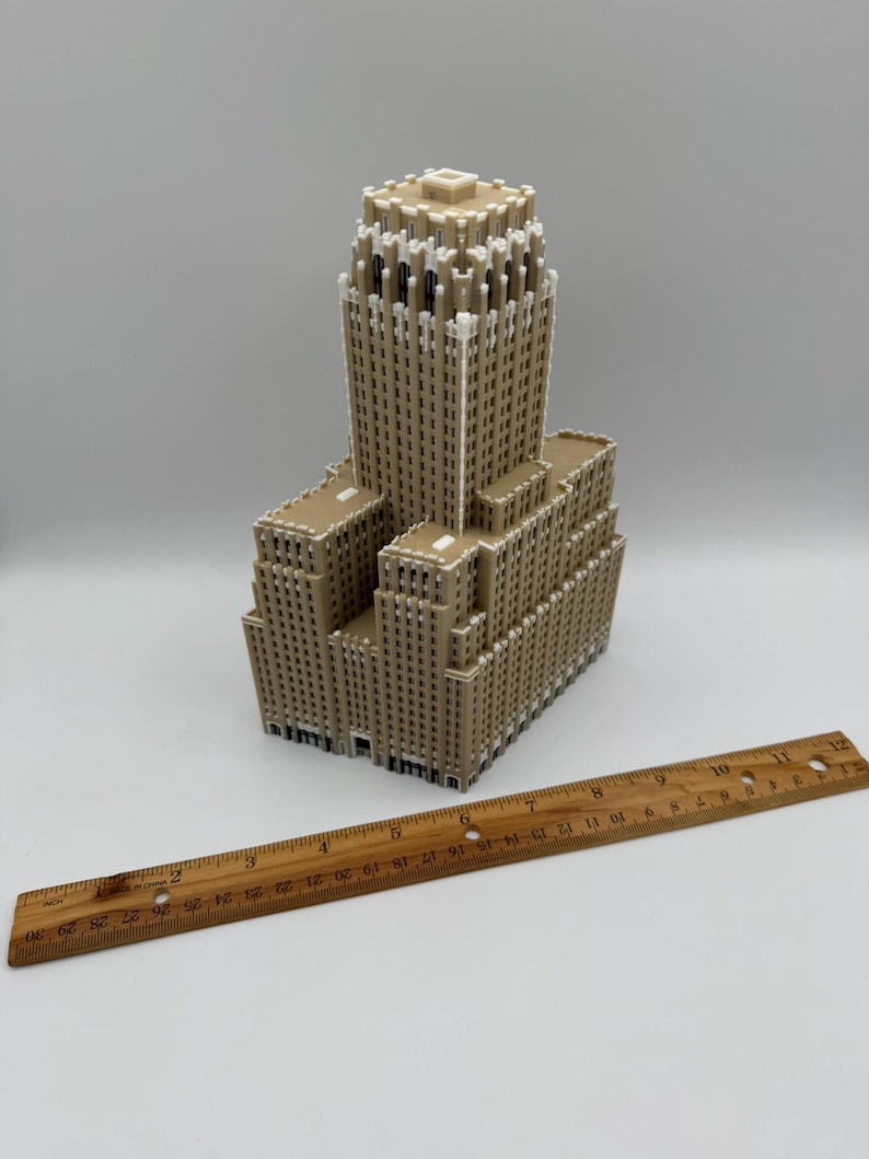 May include: A tan-coloured miniature building with a detailed architectural design. The model has a tall central tower and multiple lower sections. A wooden ruler is placed next to the building, measuring up to 30 cm.