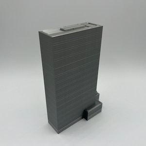 May include: A gray 3D printed model of a skyscraper with a flat roof and a small entrance.