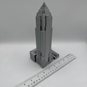 May include: A gray, 3D-printed model of a skyscraper with a ruler placed next to it. The building has a detailed facade and a pointed top. The ruler shows inch measurements.