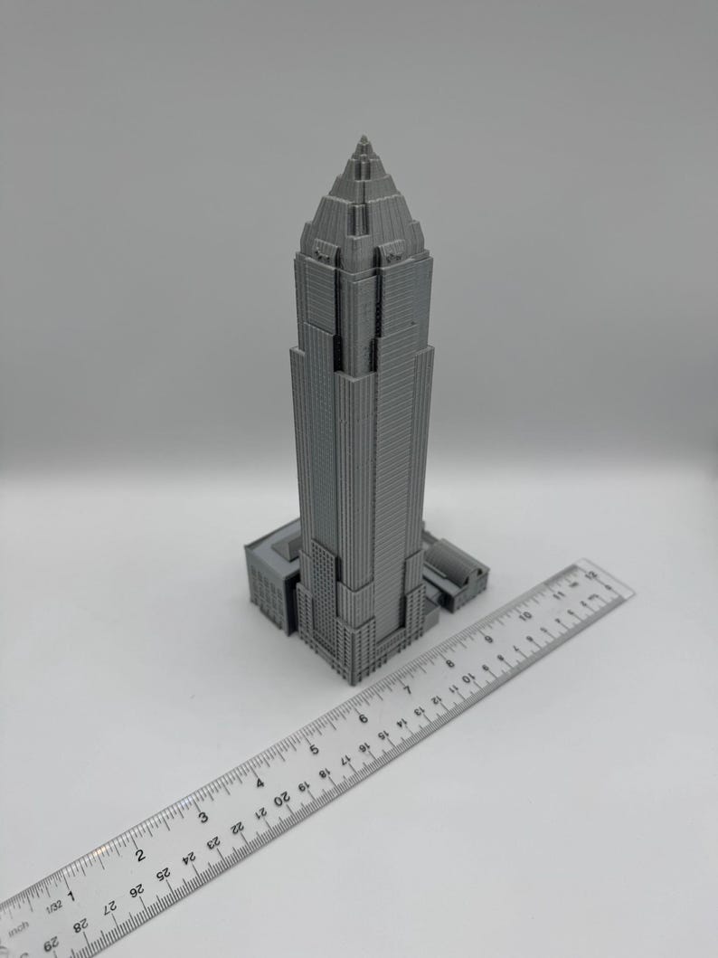 May include: A gray, 3D-printed model of a skyscraper with a ruler placed next to it. The building has a detailed facade and a pointed top. The ruler shows inch measurements.