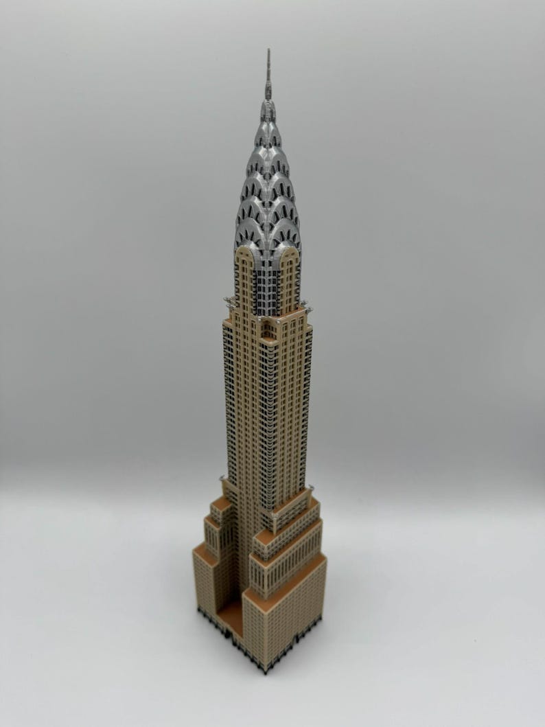 May include: A detailed miniature of the Chrysler Building, showcasing its iconic Art Deco design. The model features a tan facade, silver spire, and intricate architectural details. A collectible item, perfect for display.