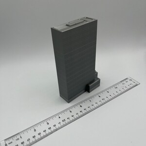 May include: A gray 3D printed model of a skyscraper building, approximately 7 inches tall, with a ruler for scale.