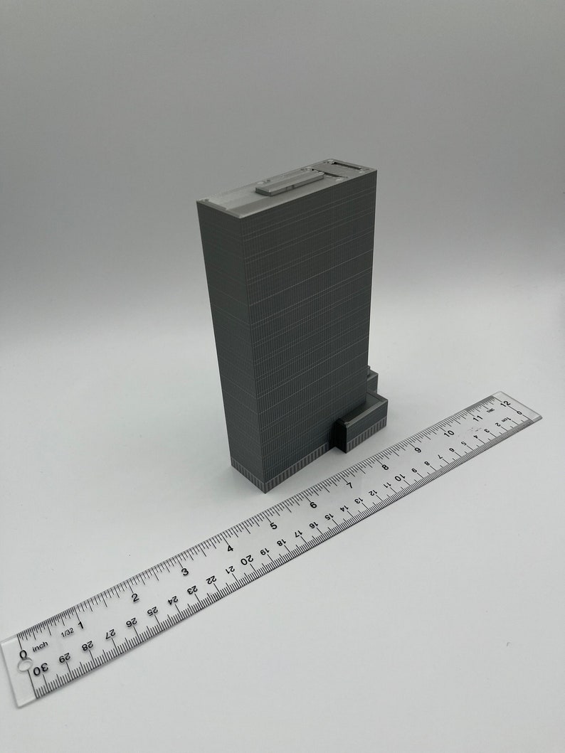 May include: A gray 3D printed model of a skyscraper building, approximately 7 inches tall, with a ruler for scale.