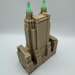 Może przedstawiać: Beżowa miniatura wysokiego budynku z dwiema wieżami zwieńczonymi zielenią. Budynek posiada wiele okien i szczeg&oacute;łowe elementy architektoniczne. Model jest prawdopodobnie repliką słynnego wieżowca.