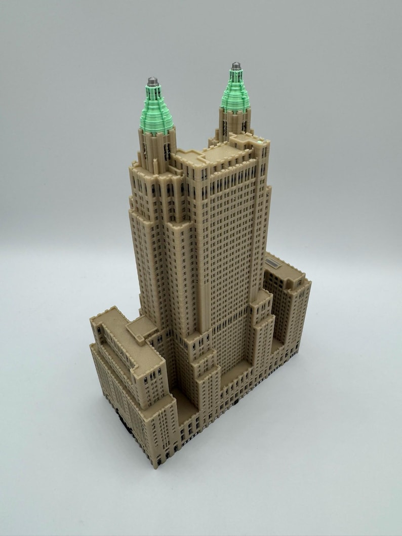 Może przedstawiać: Beżowa miniatura wysokiego budynku z dwiema wieżami zwieńczonymi zielenią. Budynek posiada wiele okien i szczeg&oacute;łowe elementy architektoniczne. Model jest prawdopodobnie repliką słynnego wieżowca.