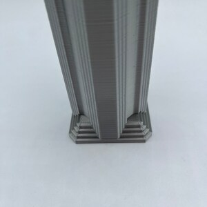 May include: A gray, 3D printed column with a square base. The base has a layered, stepped design.
