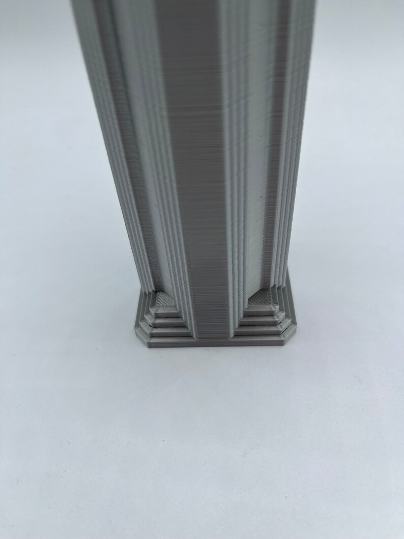 May include: A gray, 3D printed column with a square base. The base has a layered, stepped design.