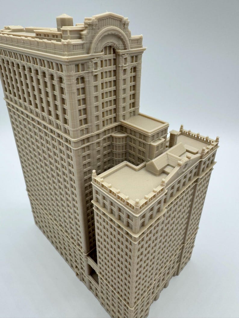 May include: A beige, detailed architectural model of a multi-story building. The model features intricate window and facade details, with a stepped design. The building has a classic, ornate style, with a flat roof.