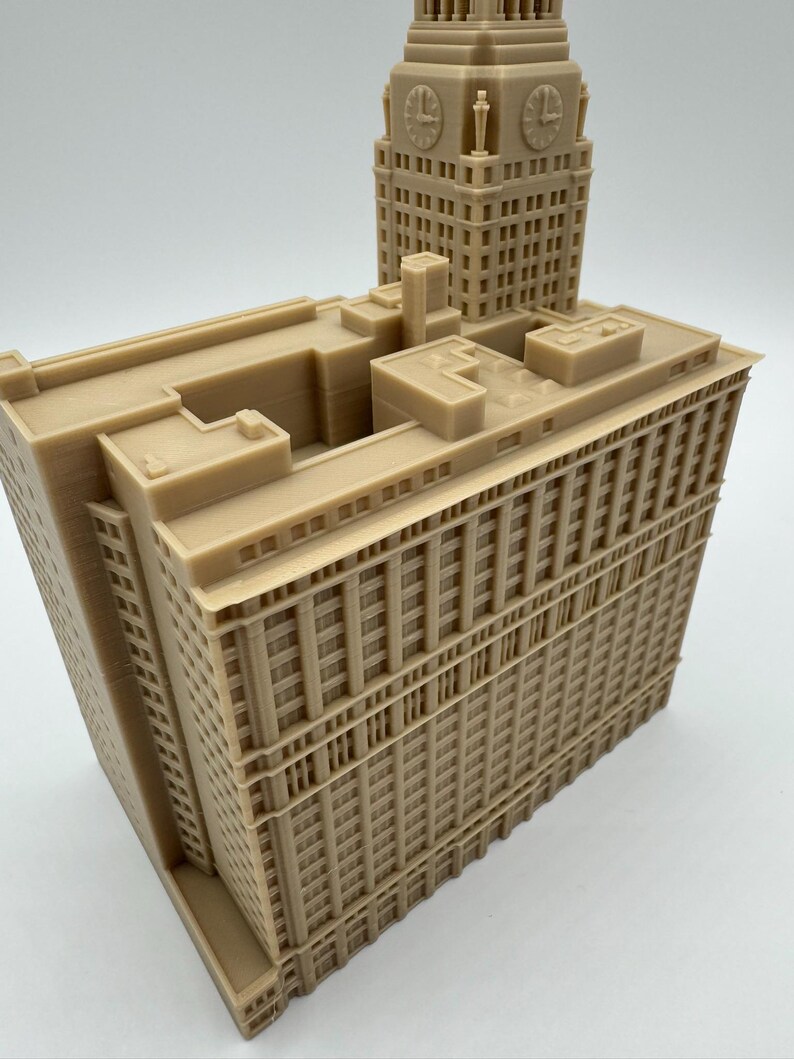 May include: A tan-colored architectural model of a building with a clock tower. The model features detailed windows, columns, and architectural elements. The clock tower has four clock faces. The building is a detailed replica.