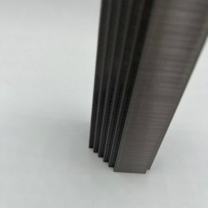 May include: A close-up of a stack of silver staples. The staples are arranged in a vertical stack and are all the same size.