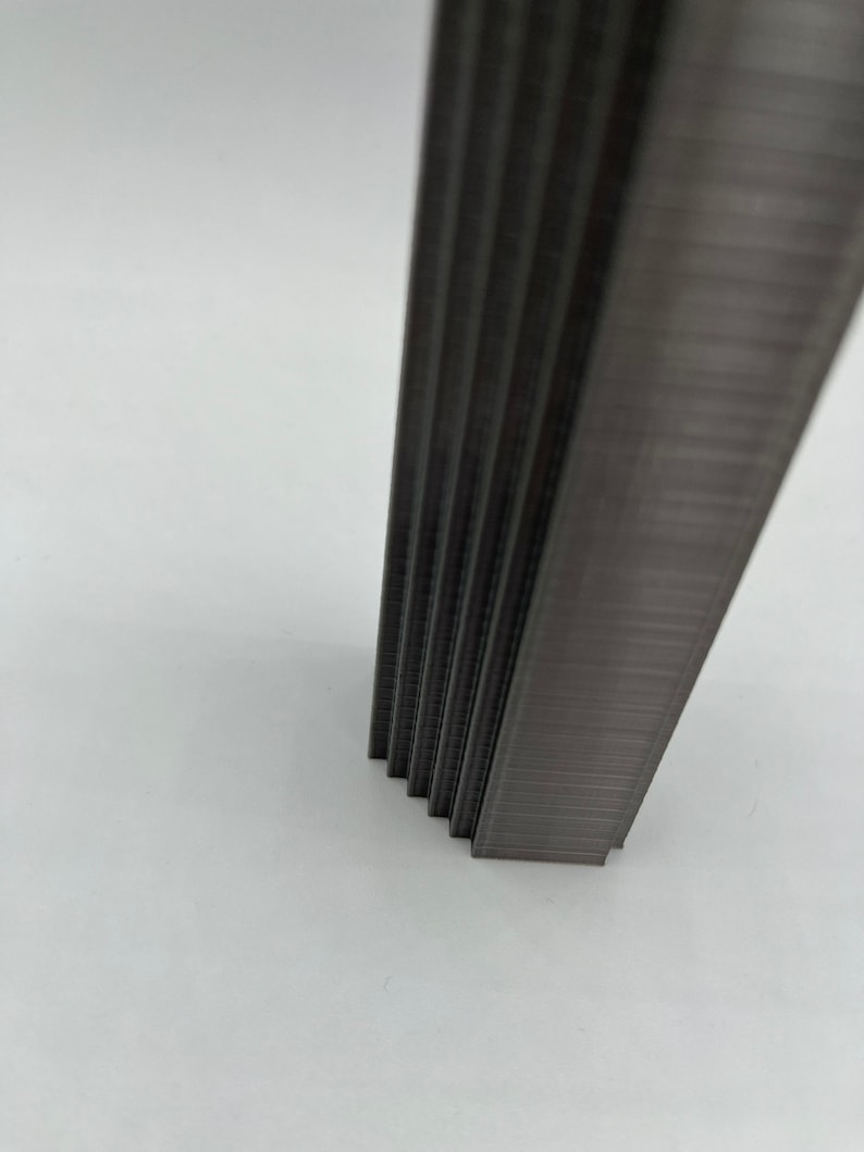 May include: A close-up of a stack of silver staples. The staples are arranged in a vertical stack and are all the same size.