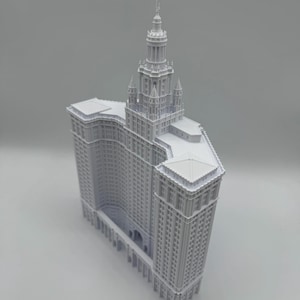 Può includere: Un modello architettonico bianco stampato in 3D del Manhattan Municipal Building. La struttura presenta un'alta torre centrale con una guglia a gradini, ingressi ad arco alla base e ali simmetriche che si estendono con motivi di finestre dettagliati.