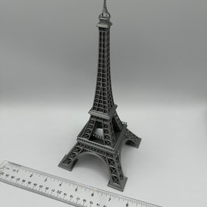 May include: A silver-colored metal model of the Eiffel Tower, a famous landmark in Paris, France. The model is approximately 8 inches tall and is sitting on a white surface.