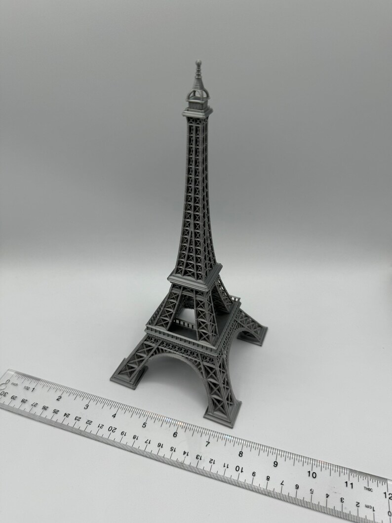 May include: A silver-colored metal model of the Eiffel Tower, a famous landmark in Paris, France. The model is approximately 8 inches tall and is sitting on a white surface.