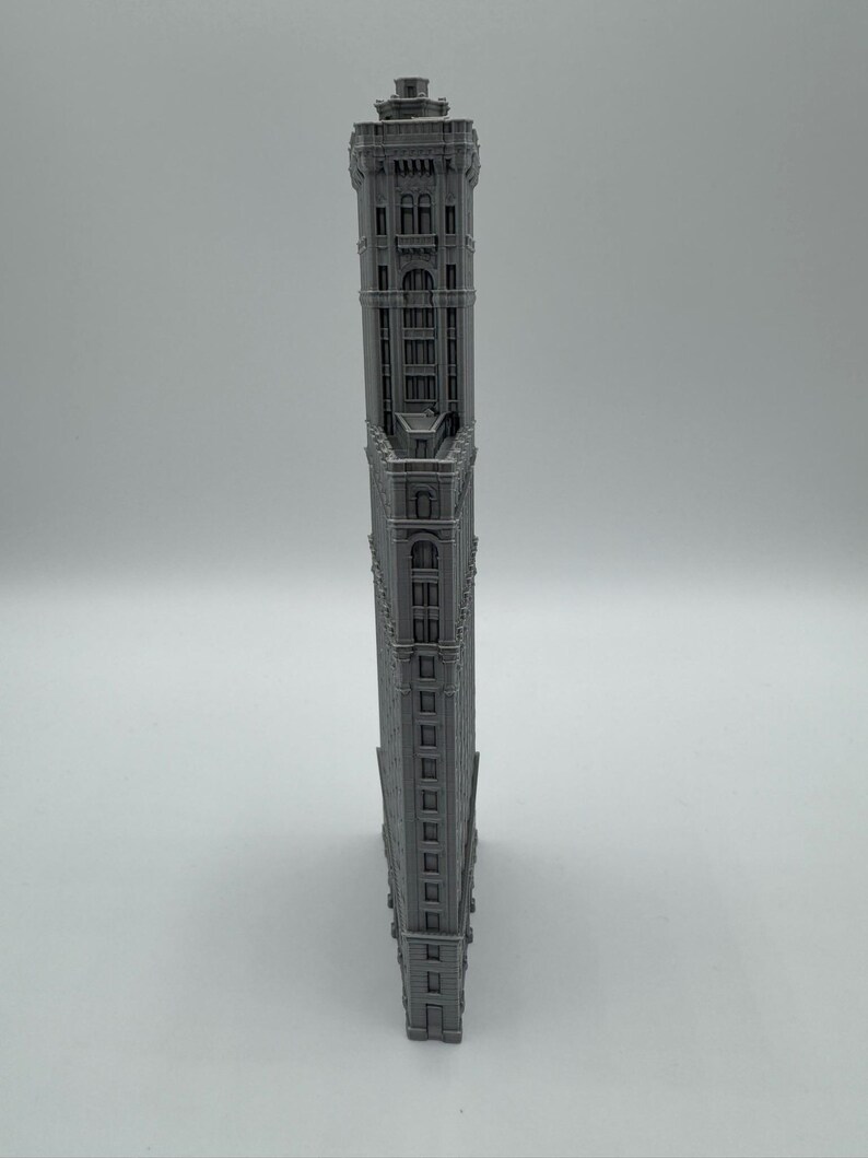 May include: A grey, miniature replica of the Flatiron Building. The model is a detailed representation of the iconic New York City skyscraper, featuring intricate architectural details and a triangular shape. The building is grey.