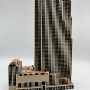 Puede incluir: Maqueta detallada de un rascacielos, con una fachada beige y numerosas ventanas negras. El edificio tiene un dise&ntilde;o escalonado, con una estructura central m&aacute;s alta y secciones adyacentes m&aacute;s bajas. El modelo mide aproximadamente 30 cm de altura.