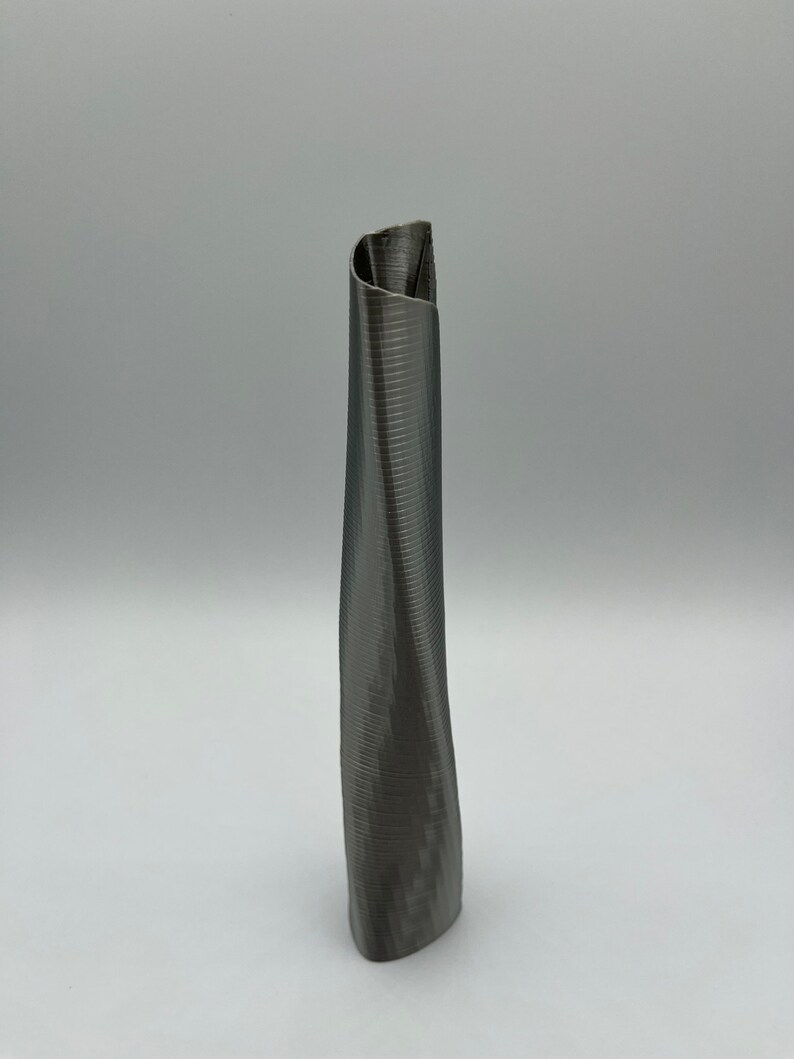 Op de afbeelding: Een grijze, 3D-geprinte vaas met een uniek, gedraaid ontwerp. De vaas is hoog en slank, met een smalle opening aan de bovenkant.