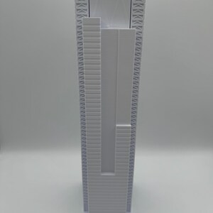 May include: A white, vertical, rectangular object with a textured surface. The object has a series of parallel lines and geometric shapes. The base is a solid white rectangle. The overall design is modern and minimalist.