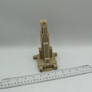 May include: A beige 3D printed model of a tall building with a pointed roof and many windows. The model is about 7 inches tall and is sitting on a white surface.