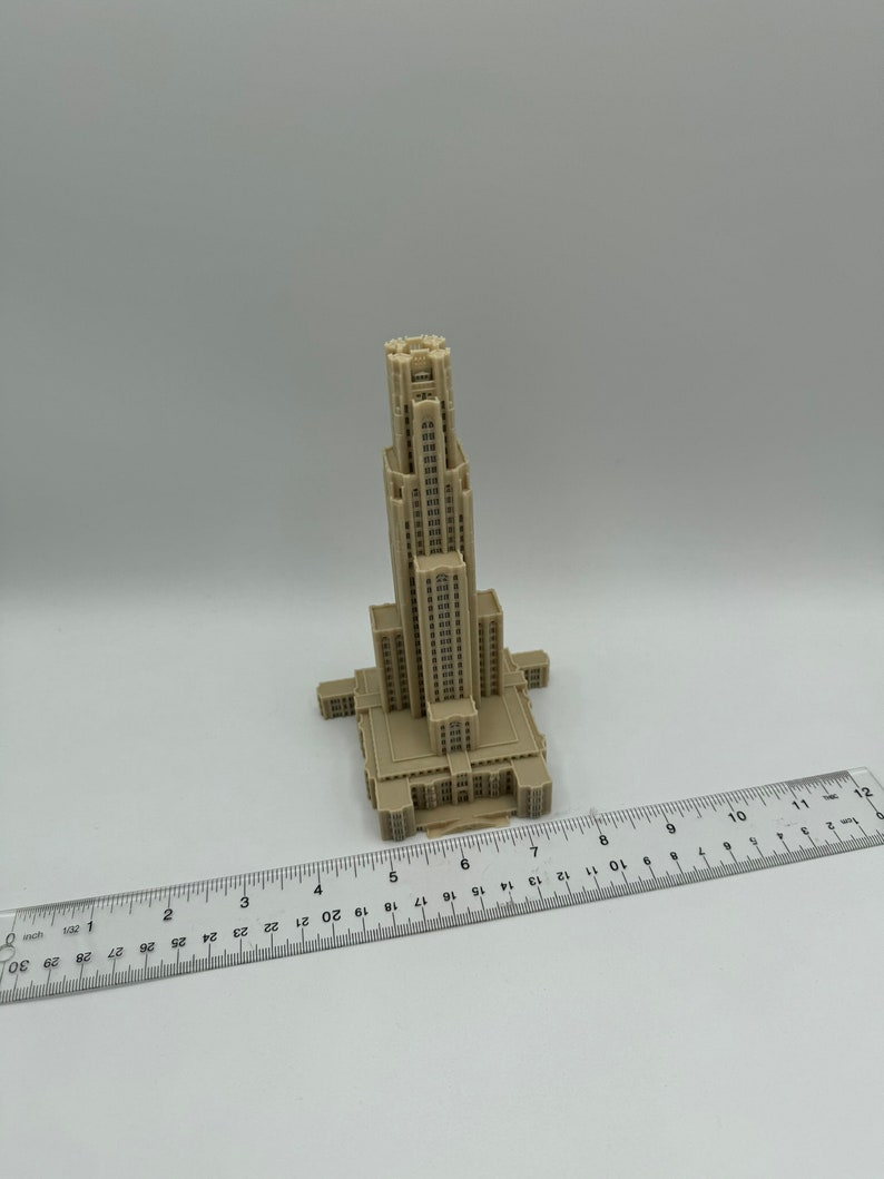 May include: A beige 3D printed model of a tall building with a pointed roof and many windows. The model is about 7 inches tall and is sitting on a white surface.