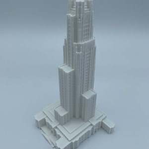 May include: A white 3D printed model of a tall building with a pointed roof and many windows. The building has a rectangular base and a series of decorative details.
