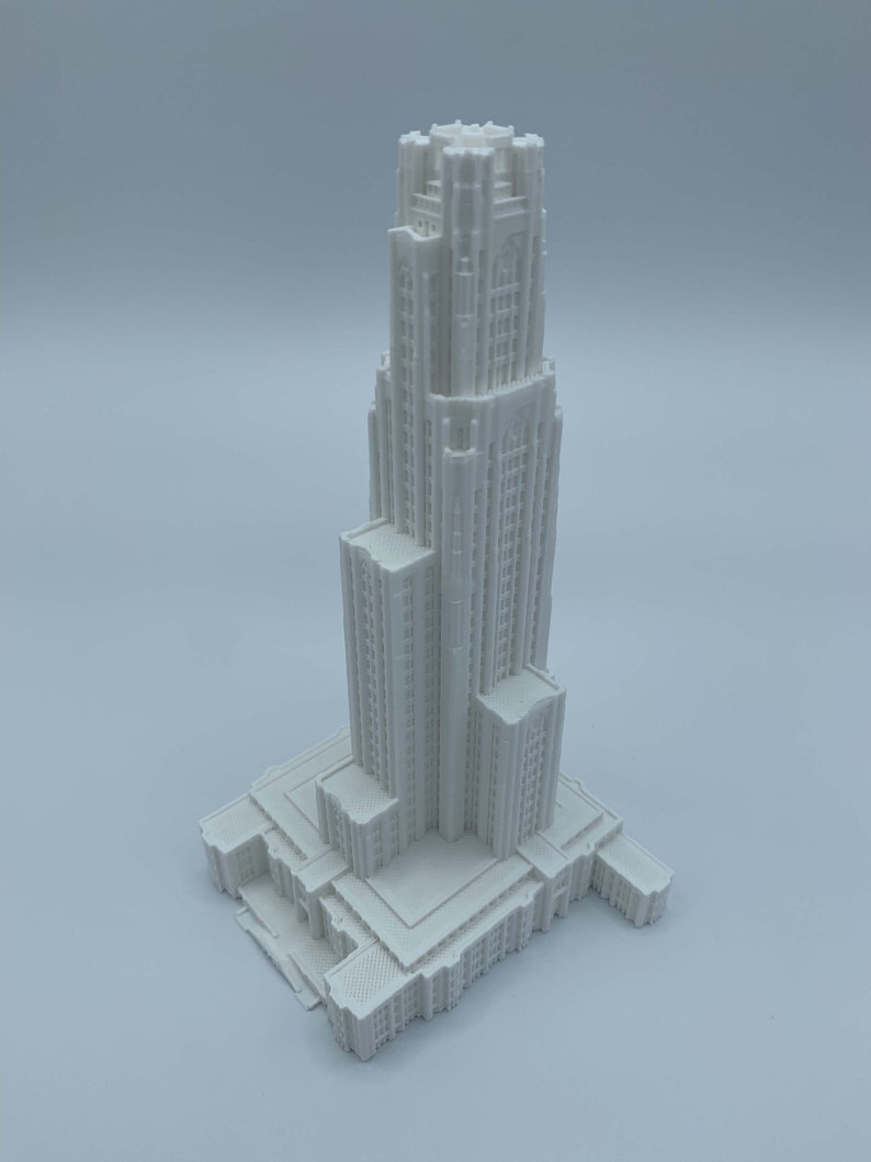 May include: A white 3D printed model of a tall building with a pointed roof and many windows. The building has a rectangular base and a series of decorative details.