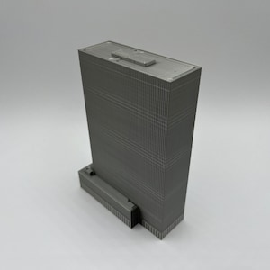 May include: A gray, detailed model of a tall skyscraper building with a flat roof. The model is made of plastic or metal and has a textured surface.