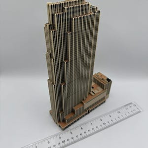 Puede incluir: Modelo detallado de un rascacielos en beige y marr&oacute;n. El edificio presenta un dise&ntilde;o distintivo con l&iacute;neas verticales y una parte superior escalonada. Una regla se coloca junto al modelo para la escala, en cm.