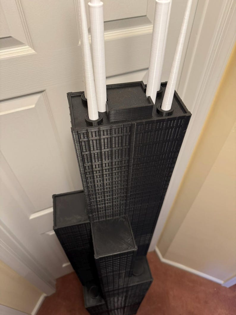 May include: A black and white 3D-printed model of a skyscraper, with detailed window patterns and white cylindrical structures on the roof. The model is a replica of a famous building.