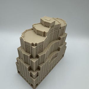 May include: A beige architectural model of a multi-storey building with a stepped design. The model features numerous windows and detailed facade elements, showcasing a classic skyscraper aesthetic. The building's structure is complex, with varying heights and setbacks.