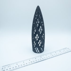May include: A black 3D printed model of a building with a diamond-shaped lattice design. The model is about 6 inches tall and is sitting on a white surface.