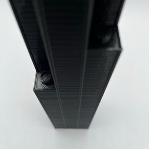 May include: A black, 3D printed model of a tall, slender building with a textured surface.