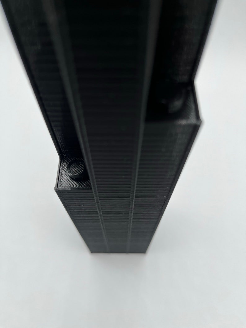 May include: A black, 3D printed model of a tall, slender building with a textured surface.