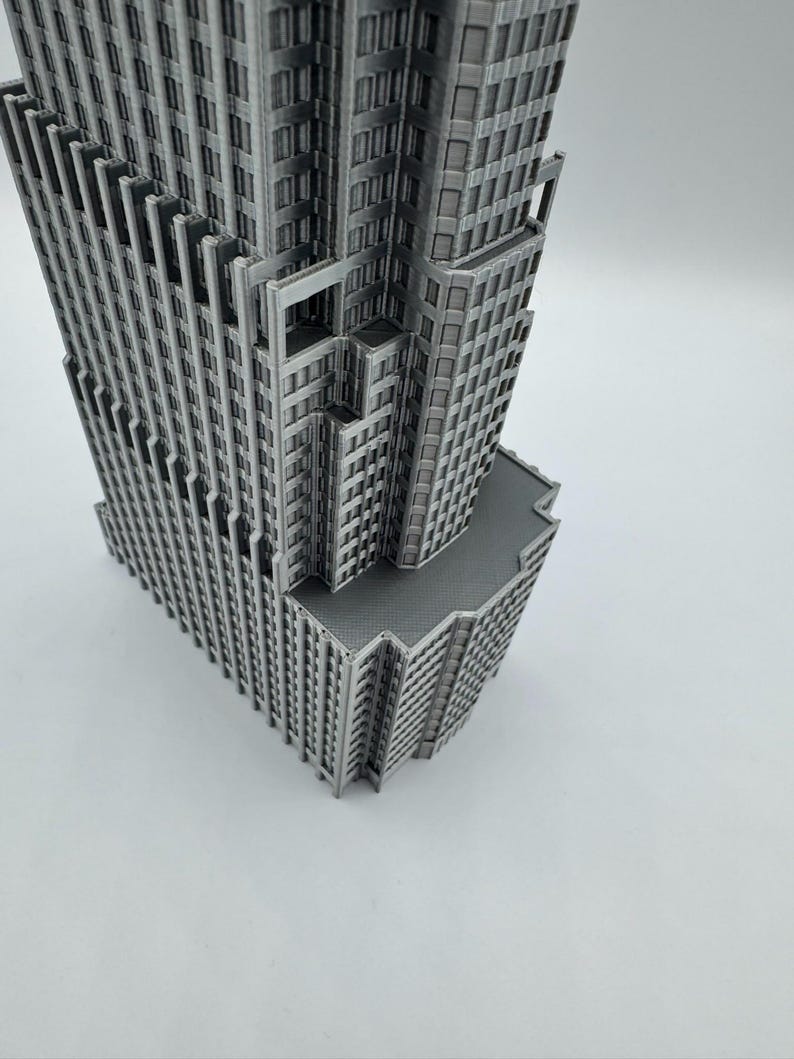 May include: A detailed, gray miniature skyscraper model. The building features multiple levels, windows, and architectural details. The model is set against a plain white background, highlighting its intricate design.