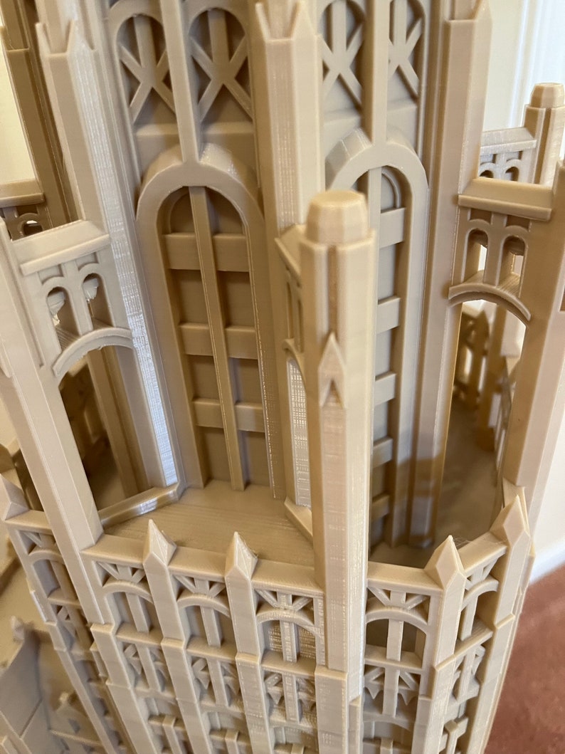 May include: A detailed 3D printed model of a tall building with intricate architectural details, including pointed arches, windows, and a spire. The model is made of a light beige plastic and appears to be a replica of a historic building.