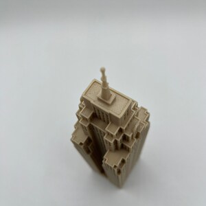 May include: A beige 3D printed model of a skyscraper with a pointed roof.